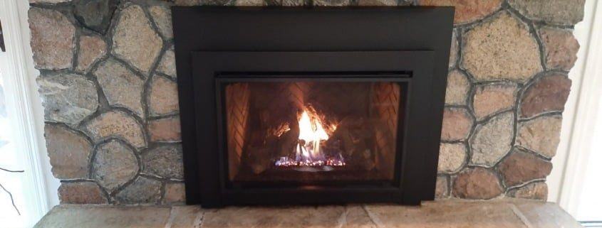 A gas fireplace insert burning in a stone surround