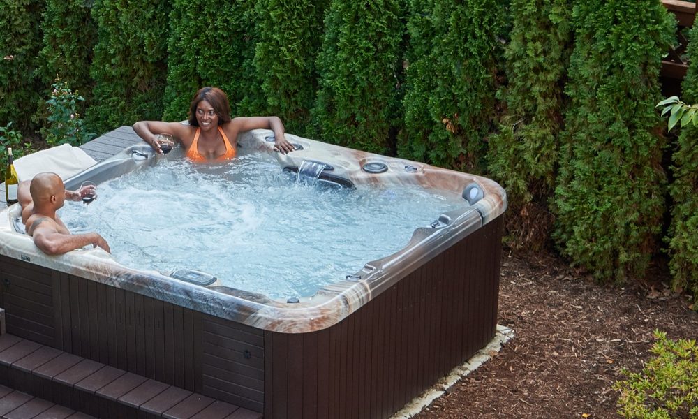 An Aspen spa with matching steps set into a garden beside a flagstone path, with two people relaxing in it