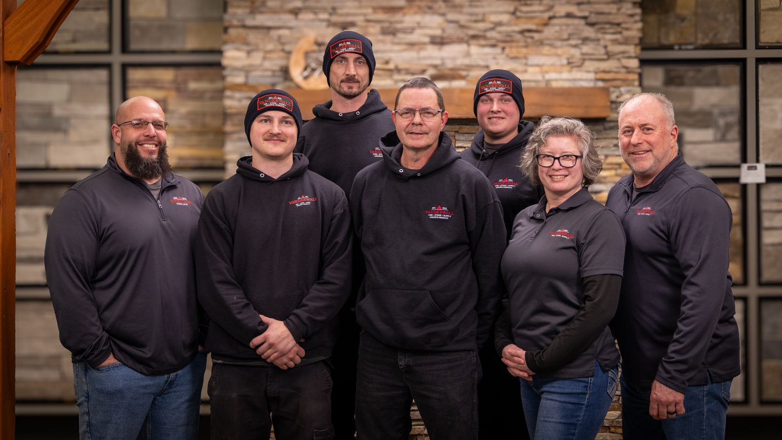 Seven members of the VanderWall team in branded fleeces and hoodies, in front of a stone fireplace