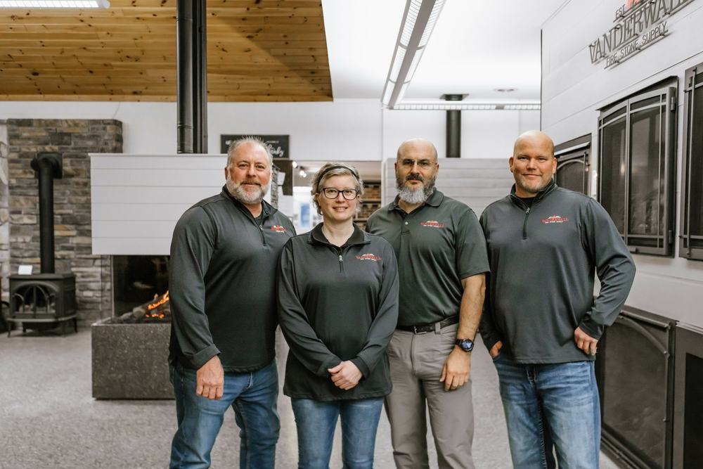 Four members of the VanderWall team in the showroom, with fireplaces and stoves behind them
