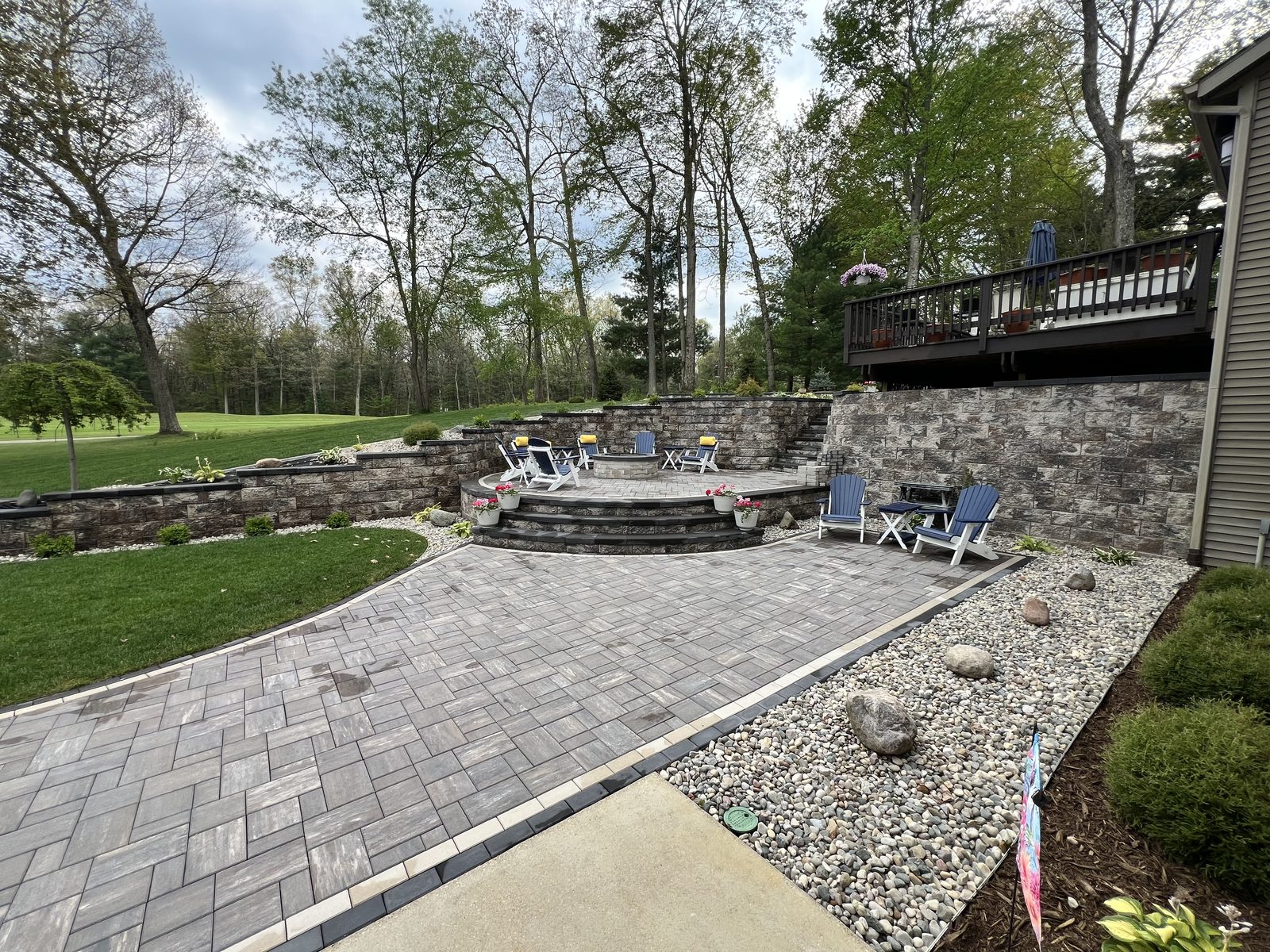 Paver patio with a fire pit, seating and a tiered wall behind it