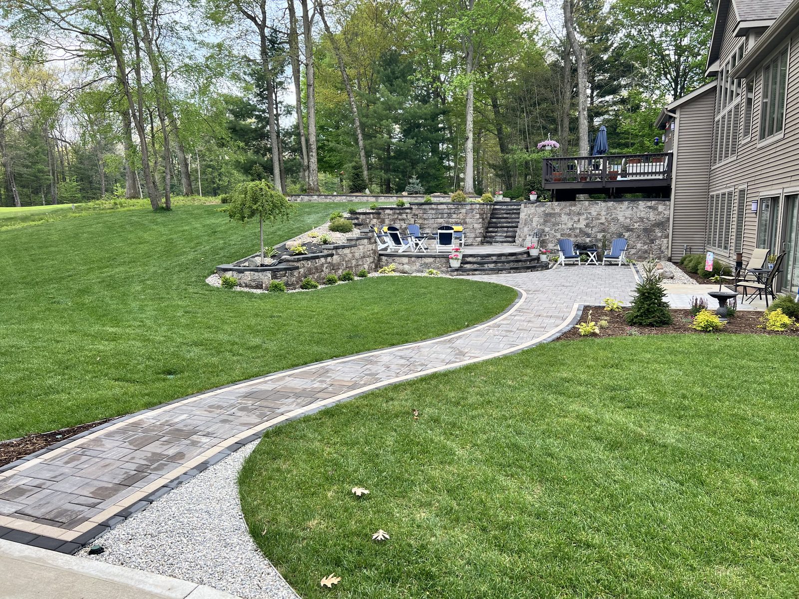 Curved paver walkway leading to a tiered retaining wall and patio